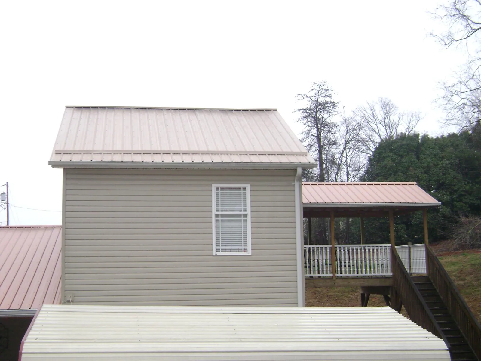 Tan metal roofs on a two story addition and attached porch, from a Roof Replacement job in Shelbyville